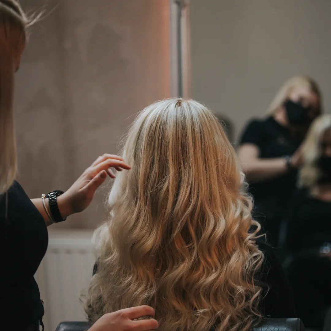 Profissional modelando cabelo loiro ondulado no salão